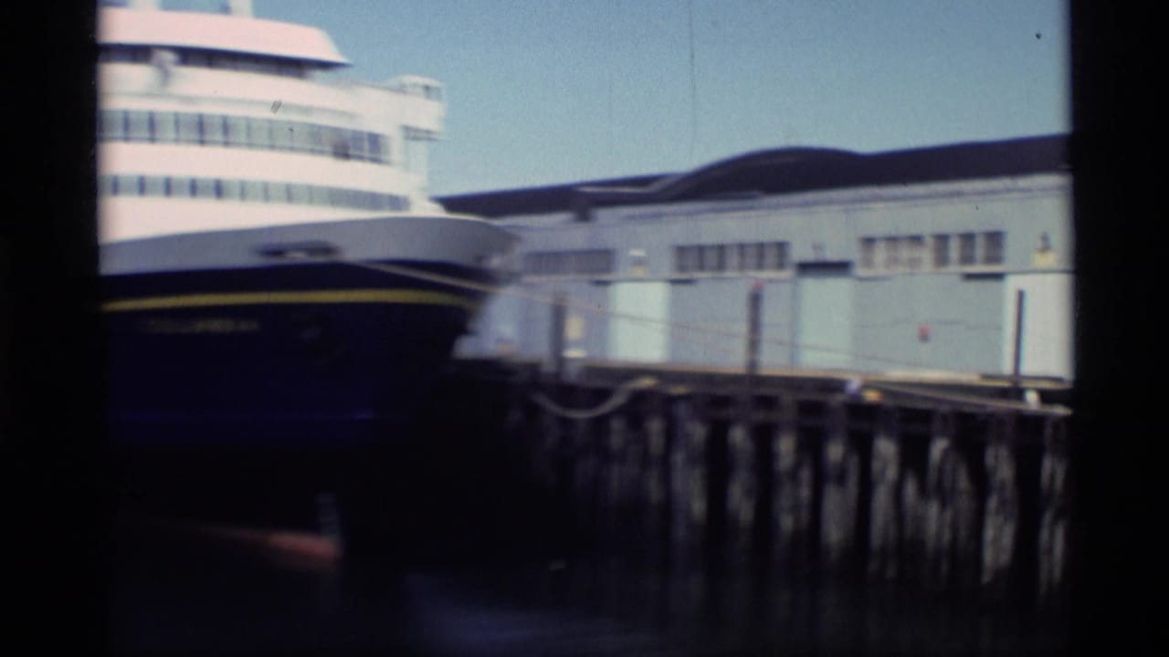 Large white-and-blue passenger vessel appears moored at an Alaska pier in 1977 Super 8 footage.