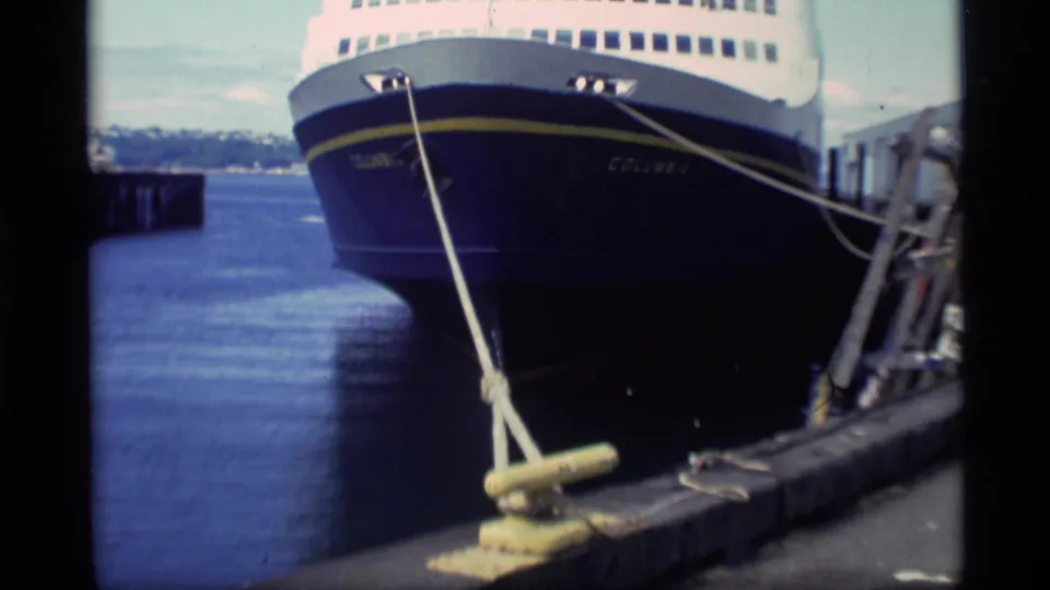 Close dockside view of the Columbia's bow, blue hull, yellow stripe, and mooring line secured to the pier.