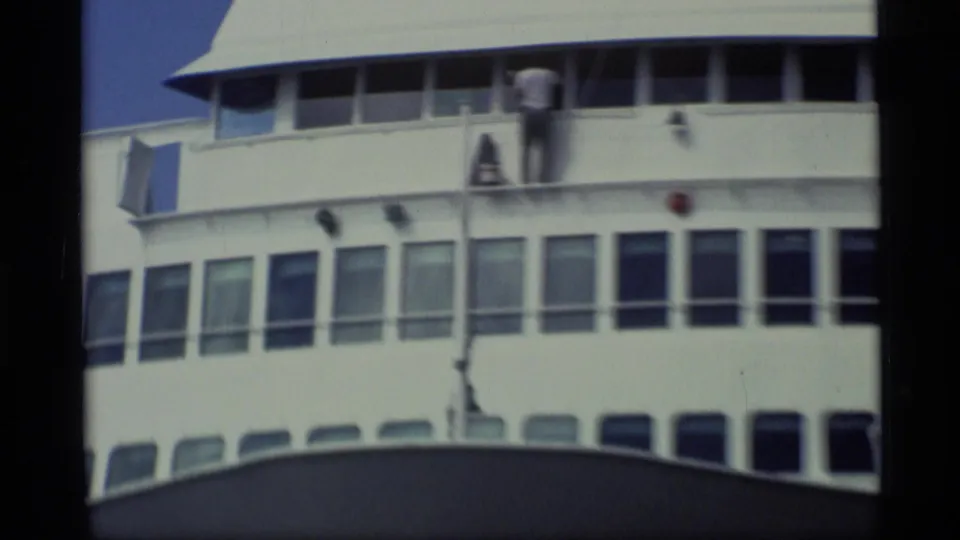1977 Alaska 8mm frame showing upper-deck windows and a crew member working near the rail of the docked ship.