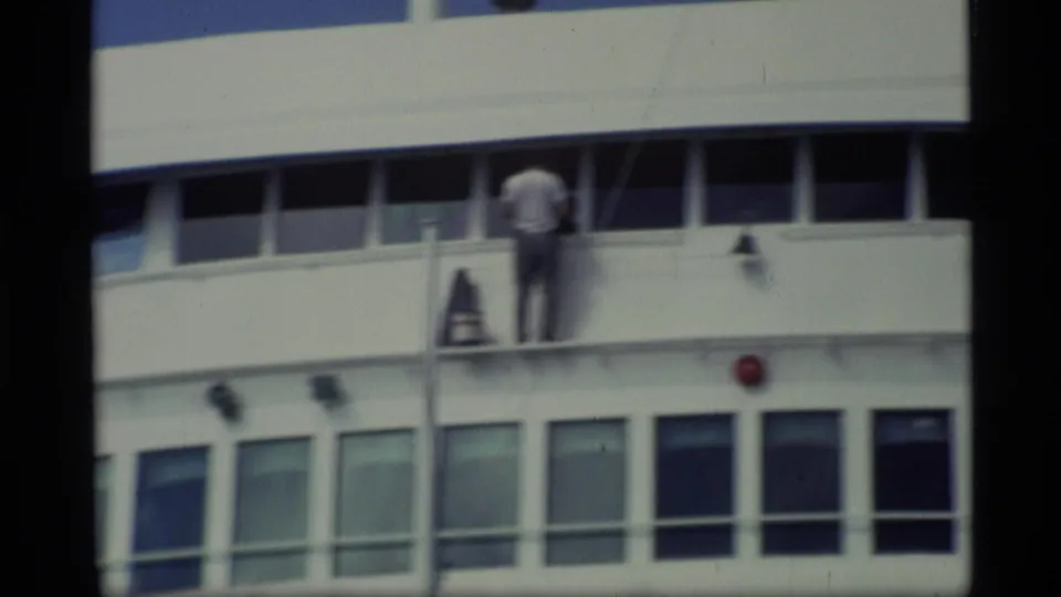 1977 Alaska ferry footage showing a crew member on an upper deck near rectangular windows and deck equipment.