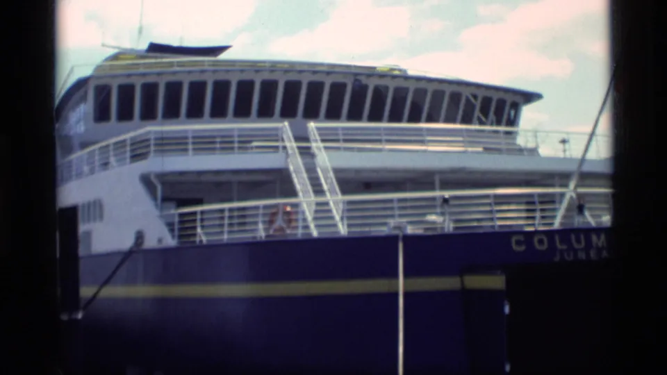 The Columbia Juneau ferry appears docked, with upper decks, railings, gangway stairs, and partial name lettering visible.