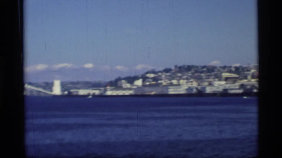 Wide 8mm harbor view with Seattle shoreline, waterfront structures, distant hills, and the Space Needle at the edge of the frame.