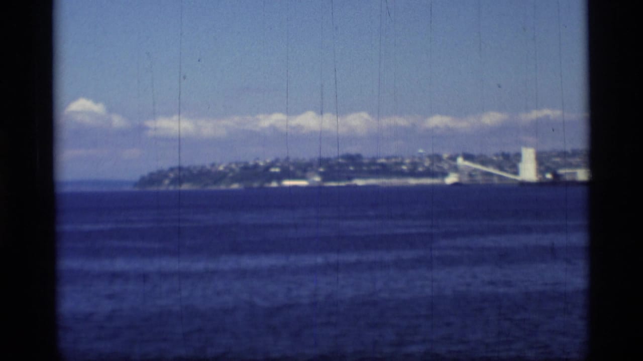 Ocean view toward a distant hillside town with a white tower near the shoreline.