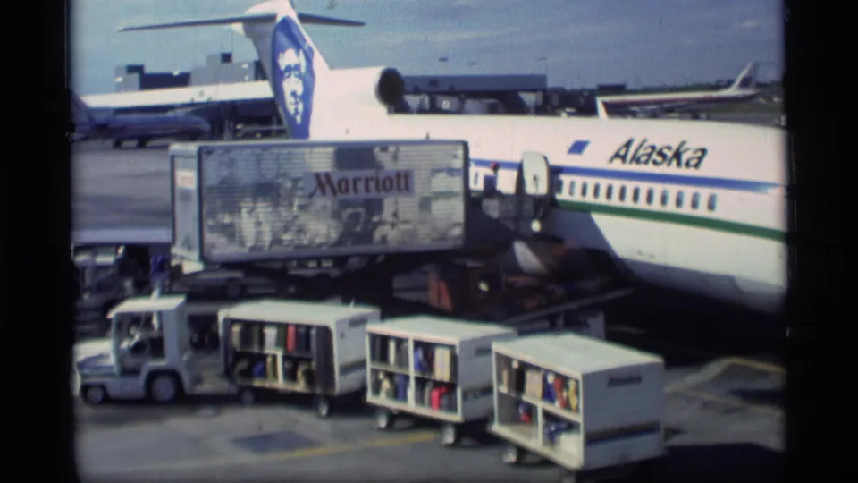1977 Ketchikan airport ramp view with an Alaska Airlines aircraft at the gate and baggage equipment positioned below.