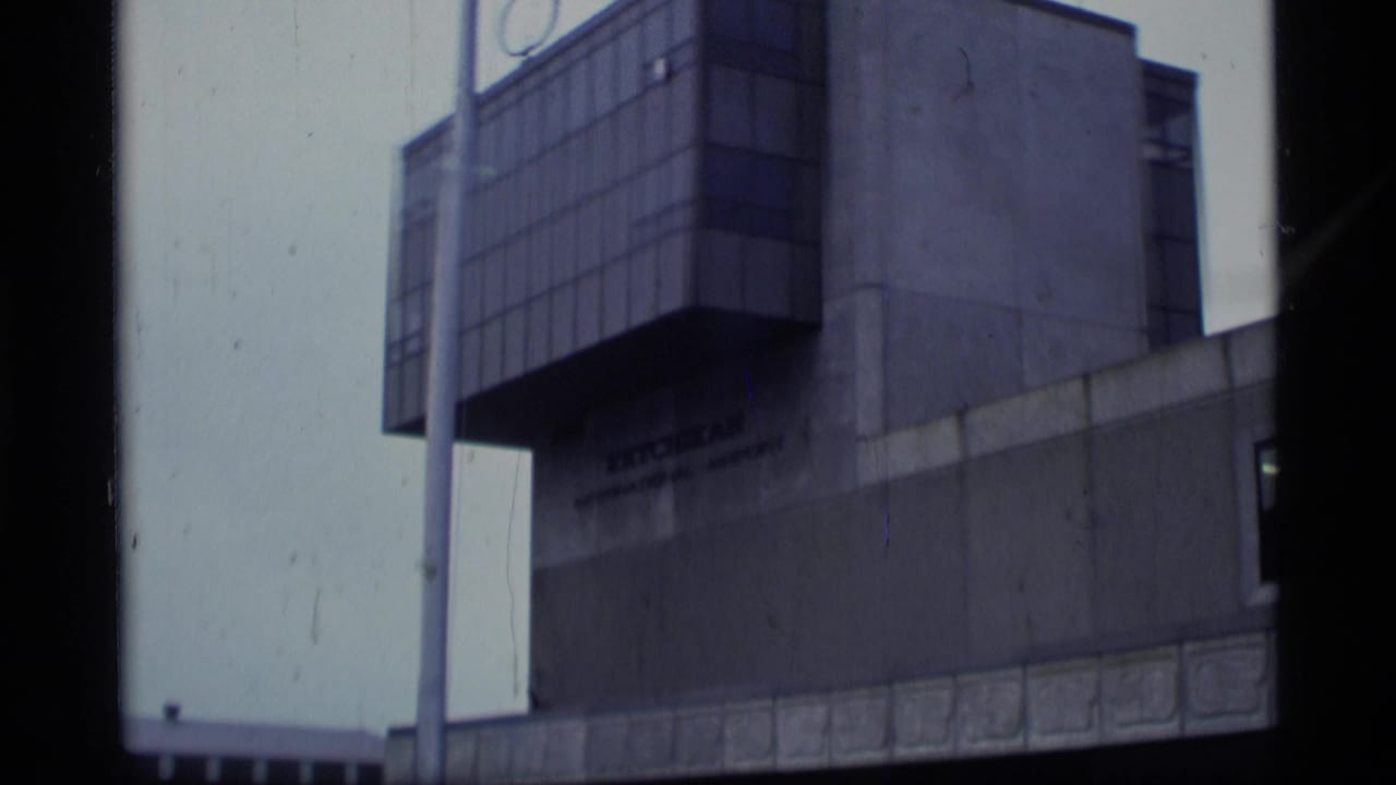 1977 Alaska 8mm frame showing an airport exterior with a modernist facade, pole, and partially visible signage.