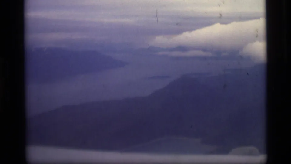 Alaska coastal landscape in soft 8mm color, showing layered mountains, water, low clouds, and dark gate borders.