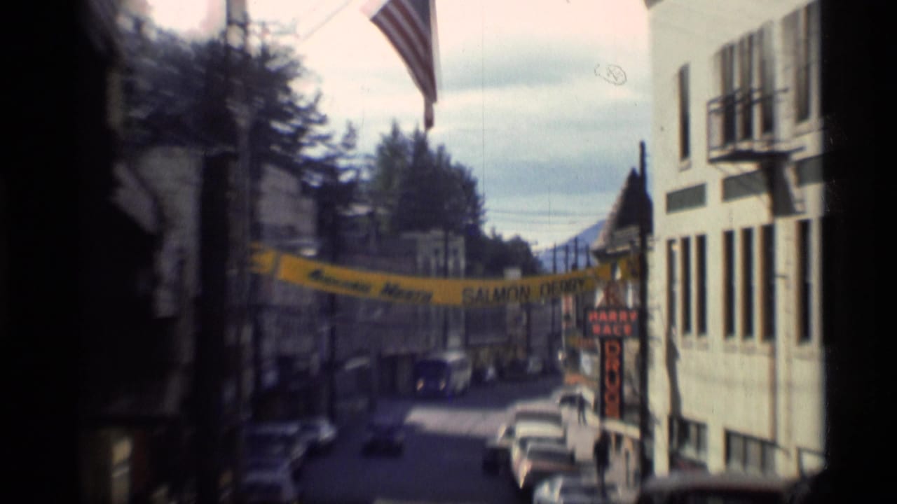 Downtown street with cars, flag, storefront signs, and a Salmon Derby banner.