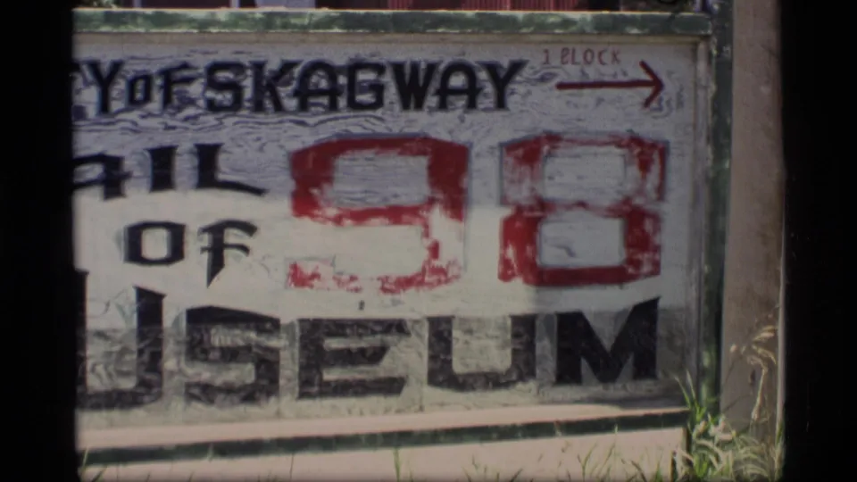 Close 1977 visitor-shot view of the Trail of 98 Museum sign in Skagway, with partial lettering and a red directional arrow.