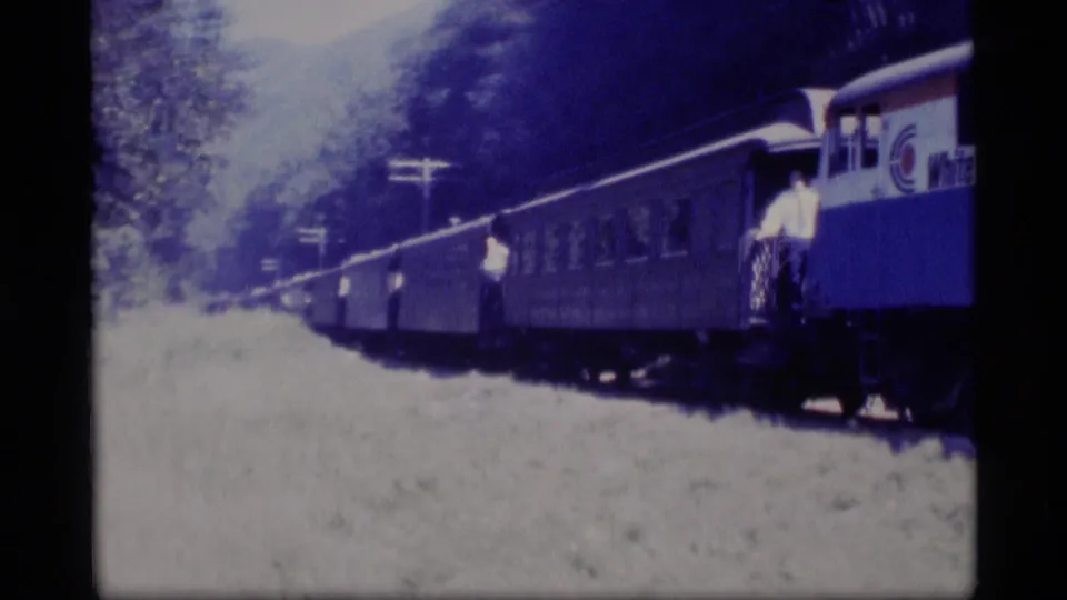 1977 Alaska 8mm frame of passenger cars passing close to camera, with people visible on the train exterior.