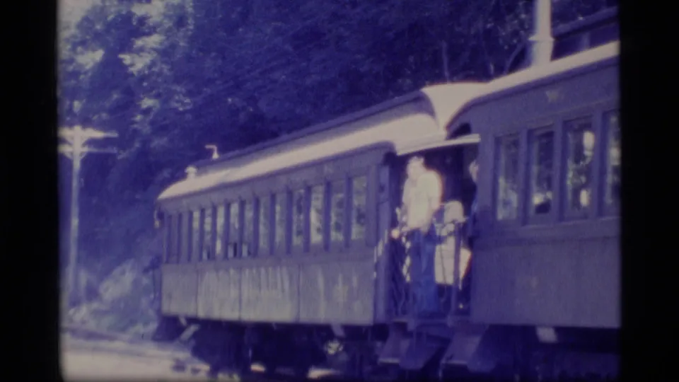 A Super 8-style frame shows the side of a passenger rail car and a man standing on the doorway steps in Alaska travel footage.