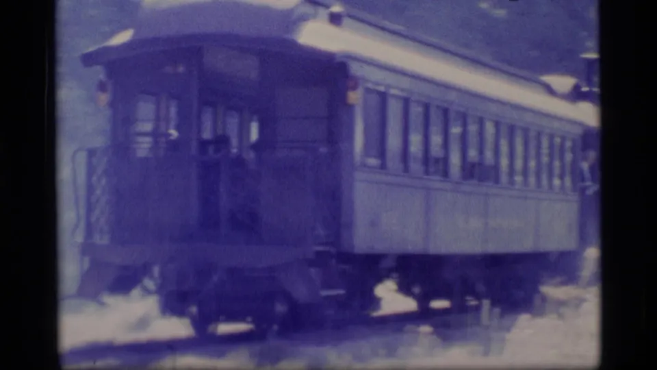 The rear or end section of the passenger train car appears in soft blue-purple 8mm footage with trees around the track.