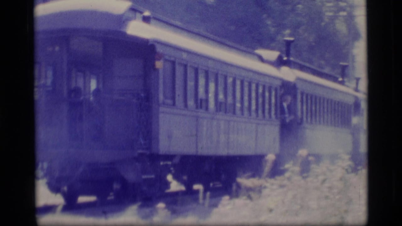 1977 Alaska 8mm frame showing passenger train cars moving past trees, with soft focus and visible film grain.