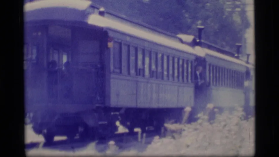 1977 Alaska 8mm frame showing passenger train cars moving past trees, with soft focus and visible film grain.