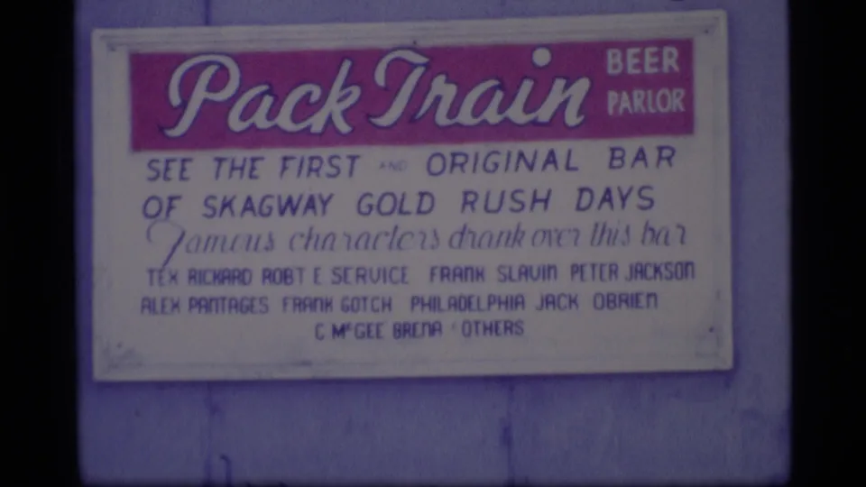 1977 Alaska 8mm frame showing a Pack Train Beer Parlor sign referencing Skagway Gold Rush days.
