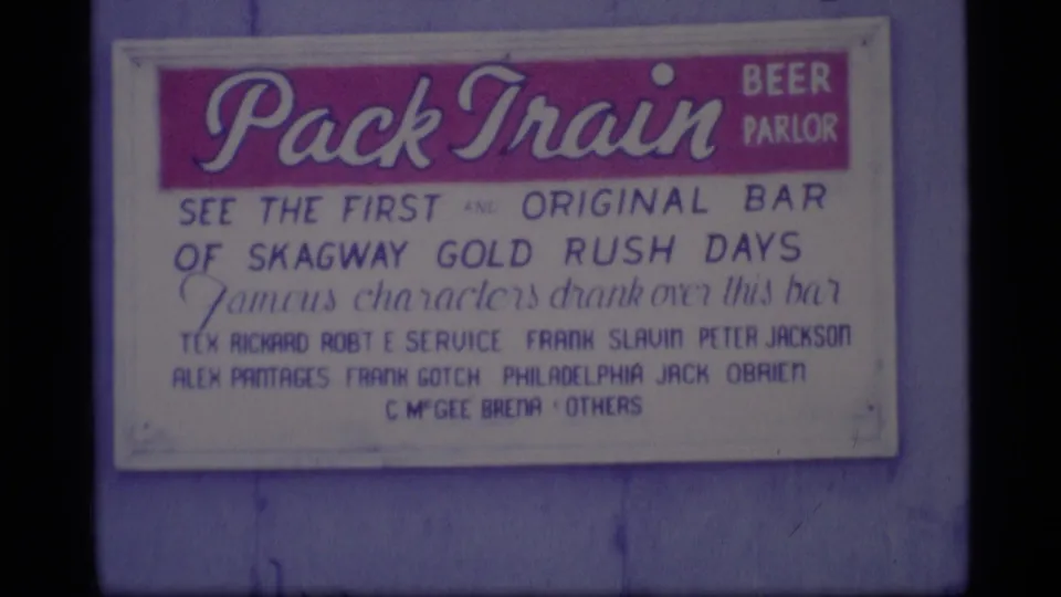 1977 Alaska 8mm frame with the Pack Train Beer Parlor sign and readable Skagway Gold Rush reference.