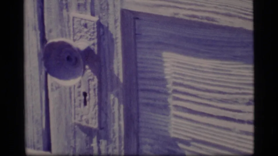 1977 Alaska home-movie frame holding on a close door detail with a round knob, keyhole, worn trim, and shuttered siding.