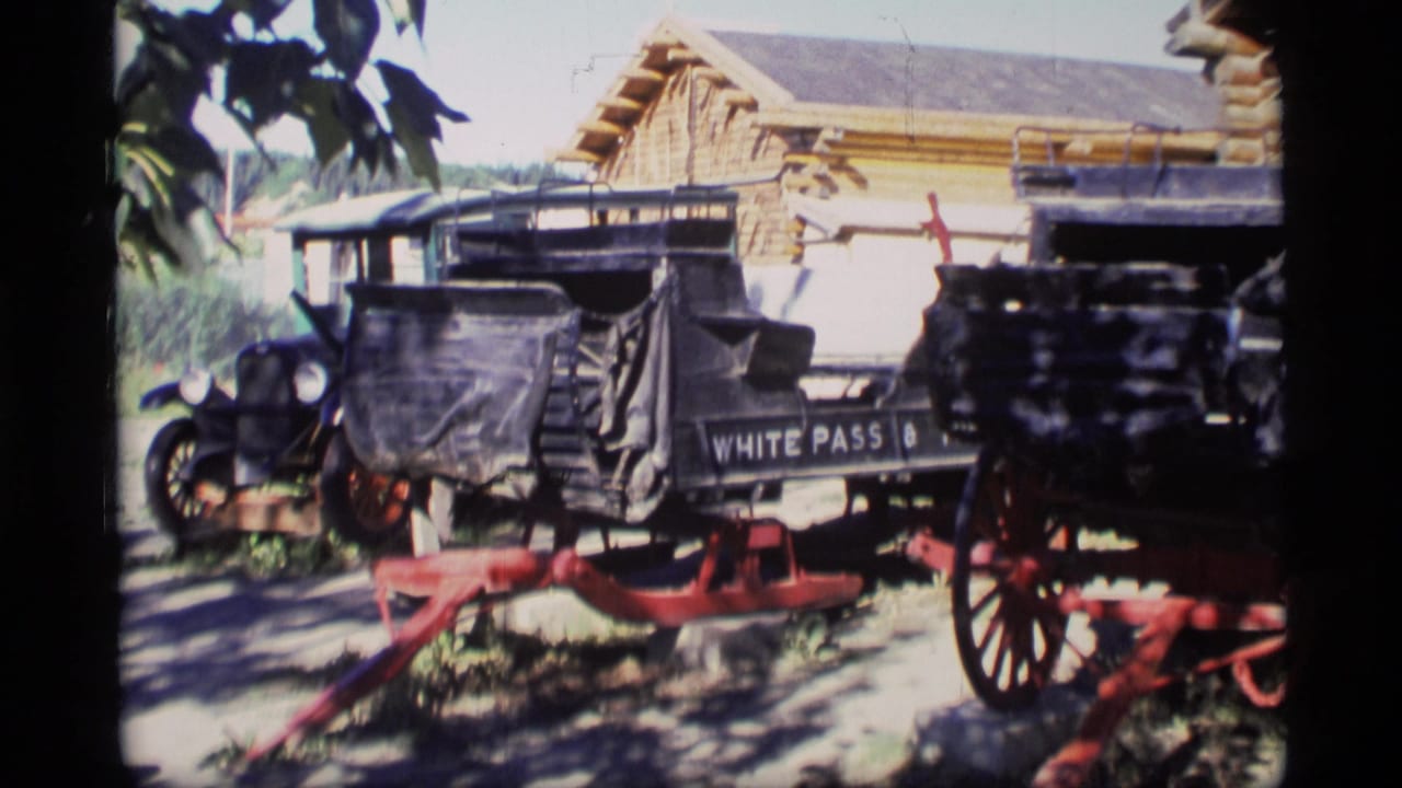 Outdoor carriage display with White Pass lettering and red wheels in front of a log building.