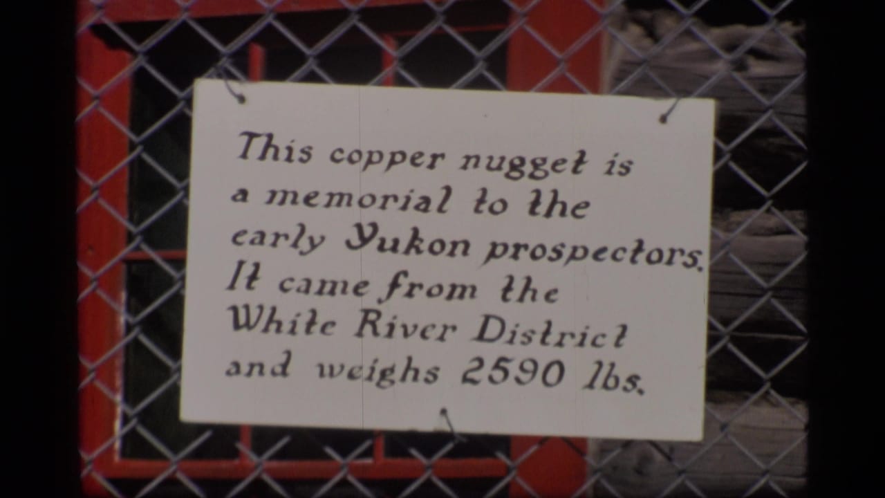 Handwritten copper nugget memorial sign on a chain-link fence.