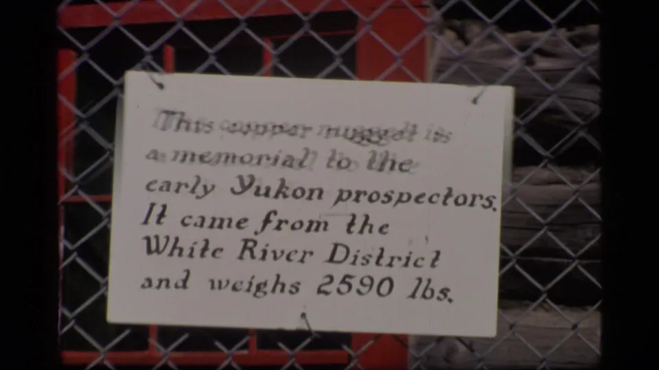 Handwritten sign behind chain-link fencing notes a copper nugget memorial to early Yukon prospectors in Alaska, 1977.