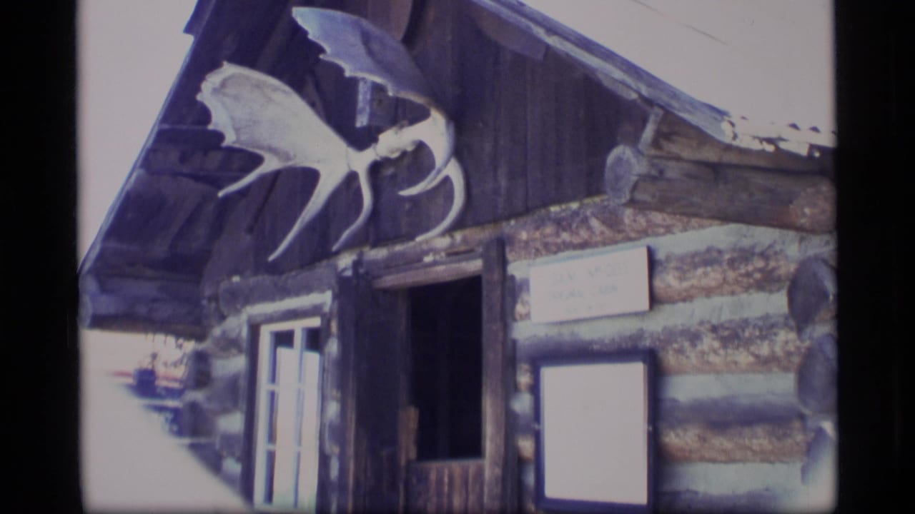Log cabin entrance with mounted antler above the roofline and posted signs near the door.