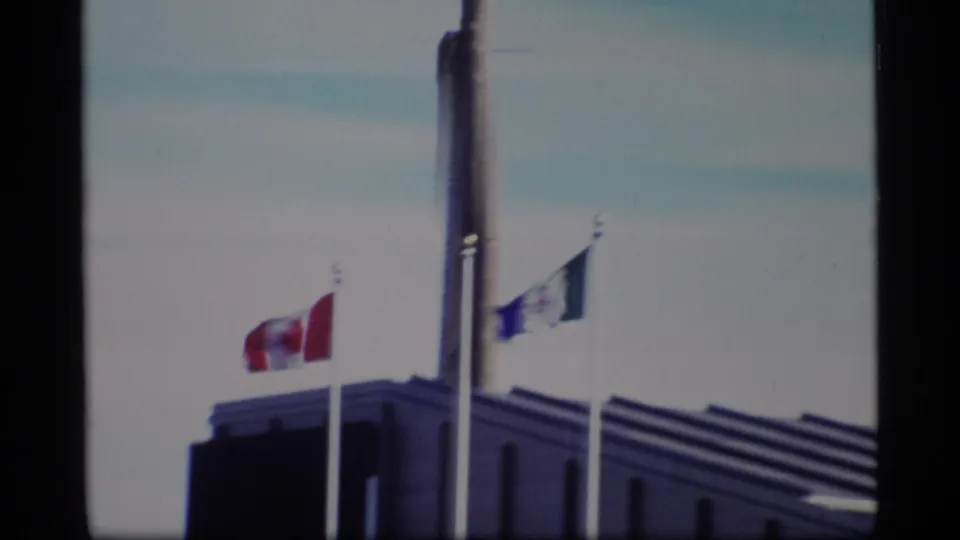 Soft 8mm frame of flags flying near a tall Yukon-marked pole over a modern building corner.