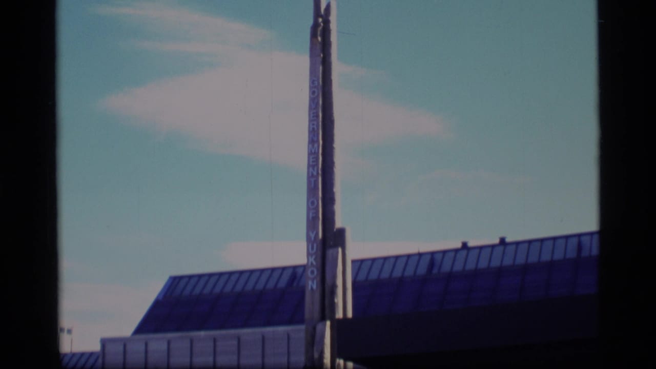 Low-angle view of a glass-roofed civic building with a vertical Government of Yukon sign.
