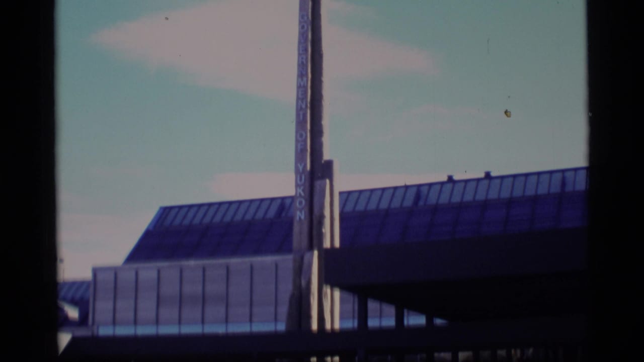 Glass-roofed building facade with vertical sign and dark film gate edges.