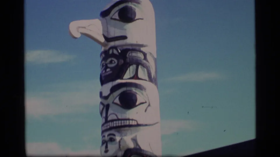1977 Alaska 8mm frame showing a close, handheld view of painted totem pole carvings against the sky.
