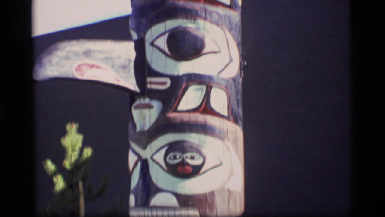Close view of the middle of a painted totem pole with bold face designs.