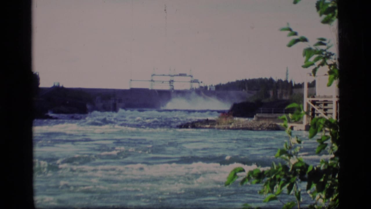 Dam gates release water into a wide river with foliage at the right edge.