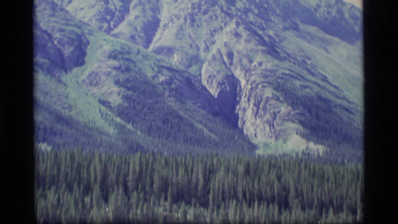 Rocky mountain slope above evergreen forest with visible film-frame border.