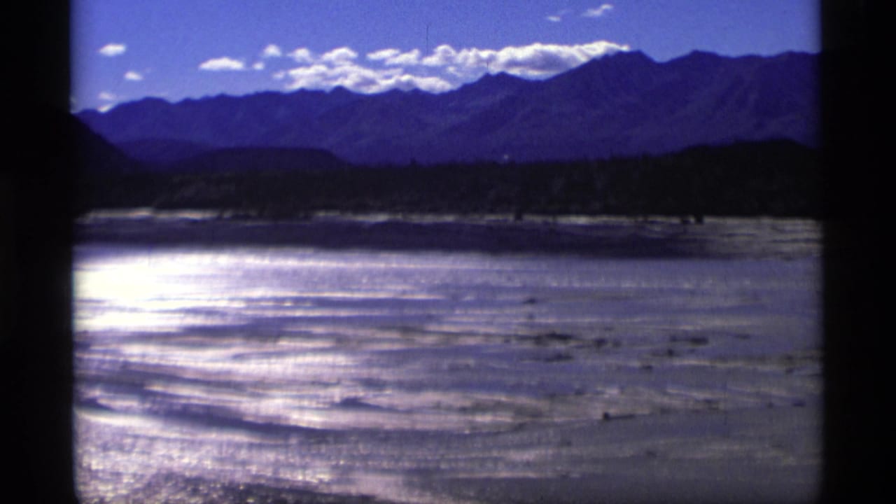 Sunlit water and sandbars stretch toward a dark tree line and high mountain ridge.