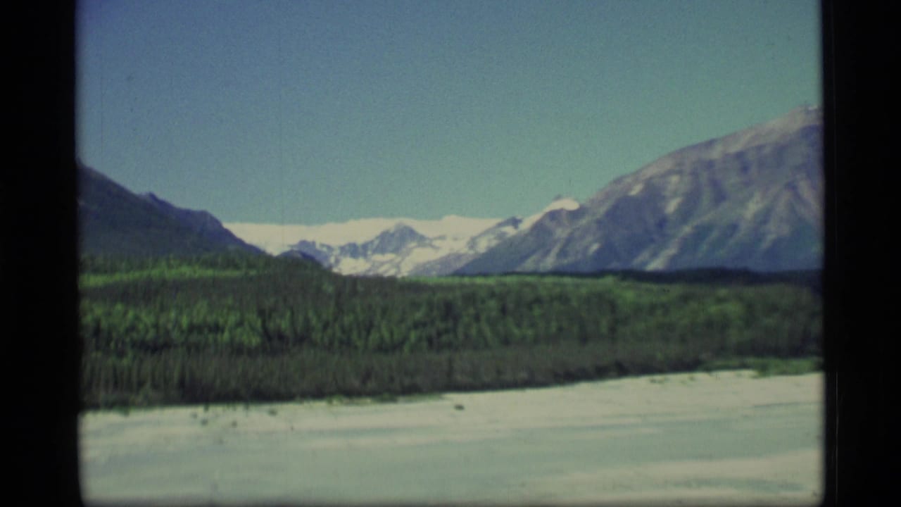 Aerial view of a frozen lake bordered by evergreen forest and snow-capped mountains.