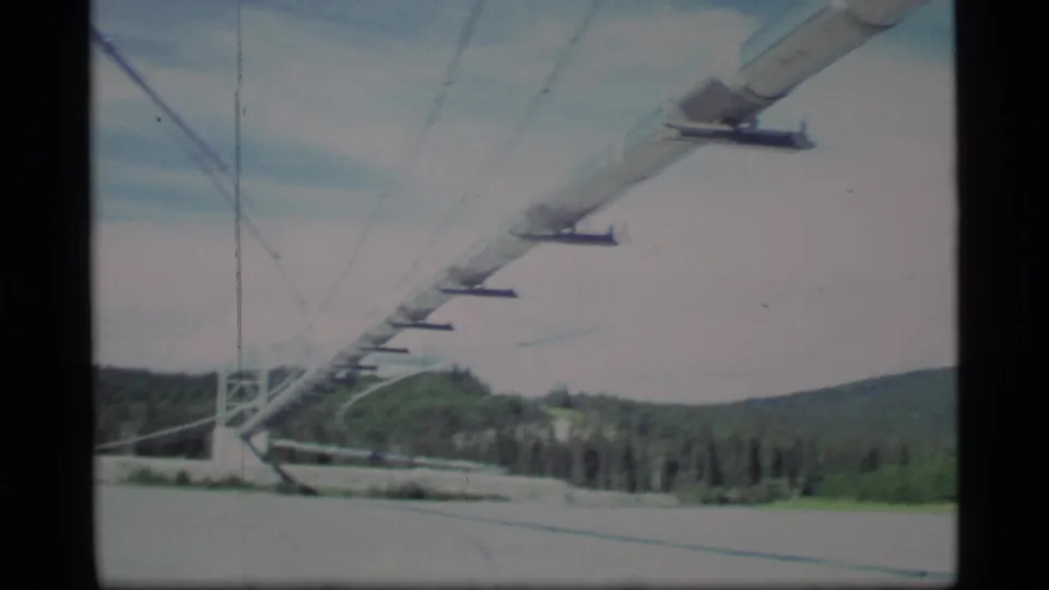 1977 Alaska 8mm close view of ski-lift cable supports over snow, with forested hills and soft vintage film color.