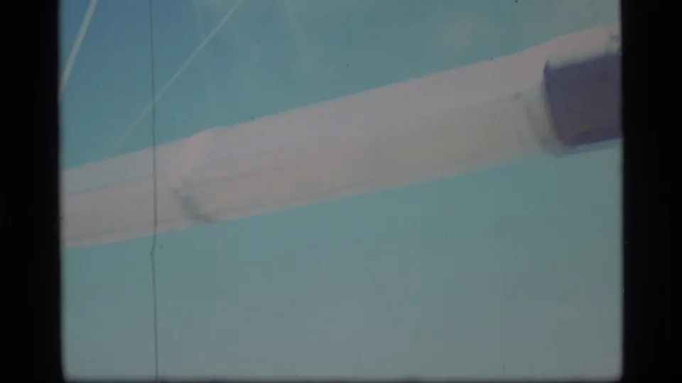 Soft 8mm close-up of a pale pipe or beam filling the frame against blue sky during the pan.