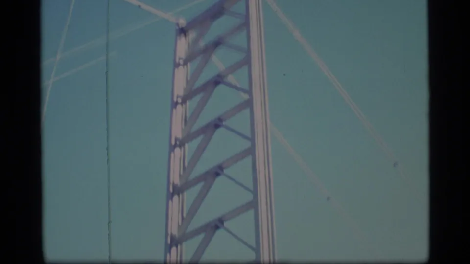 1977 Alaska 8mm frame showing the upper span of a silver lattice tower with diagonal bracing against pale sky.