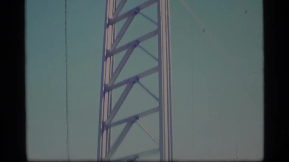 1977 Alaska 8mm frame showing the midsection of a silver tower structure, with diagonal lattice bracing filling the frame.