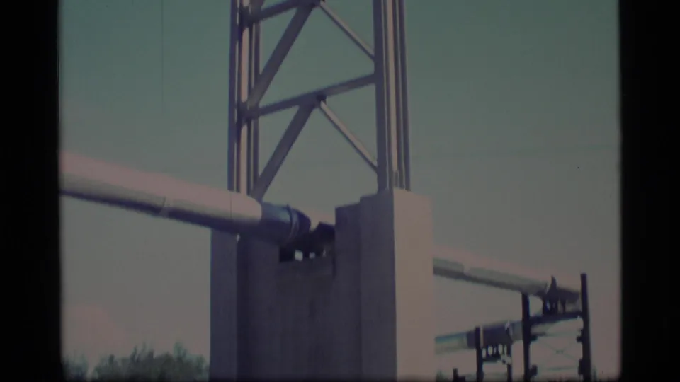 1977 Alaska 8mm frame showing the tower base area, horizontal beams, and a block-like support with sky behind it.