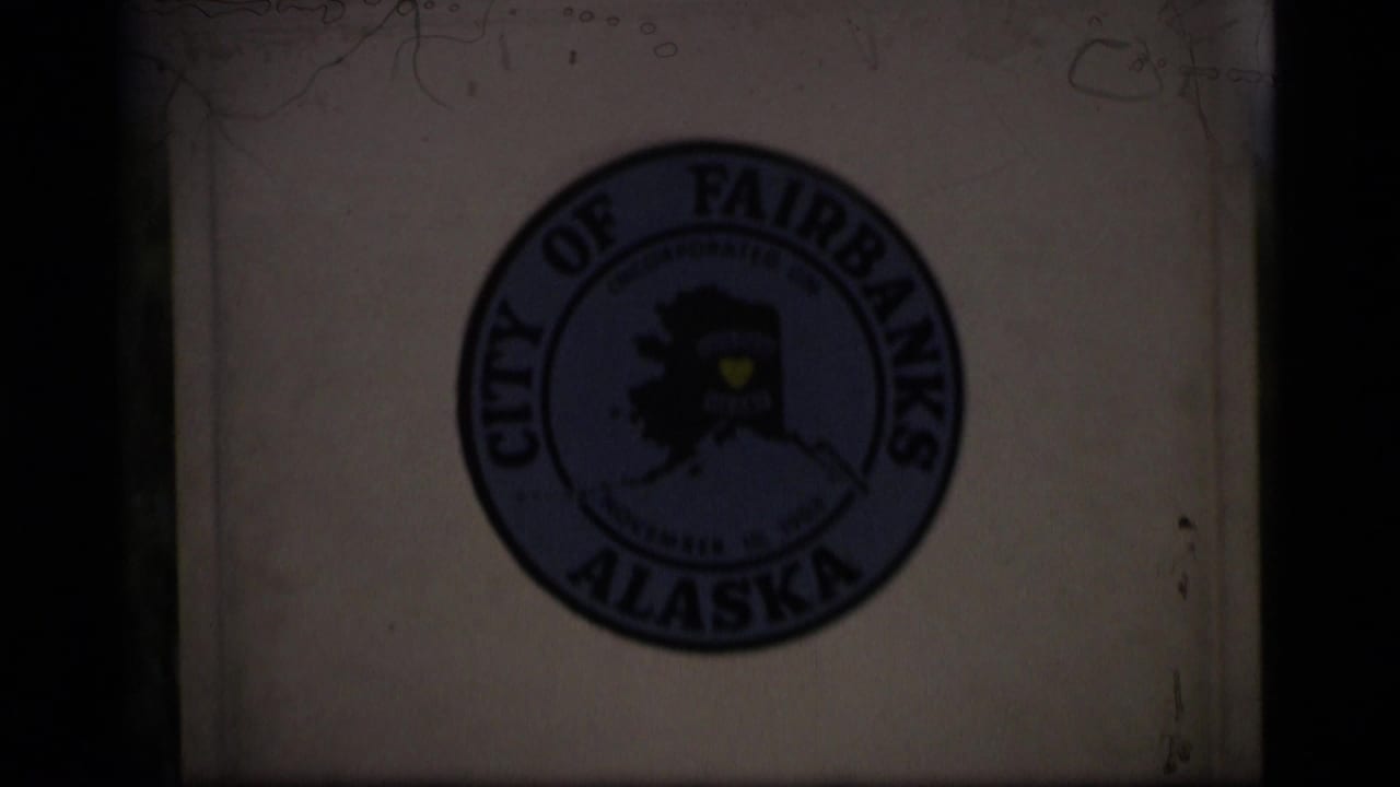 Close view of a City of Fairbanks Alaska seal on a white roadside marker.