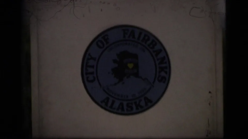 1977 8mm close-up of the City of Fairbanks Alaska seal on a white Alaska Highway mile marker, partly shadowed by the film frame.