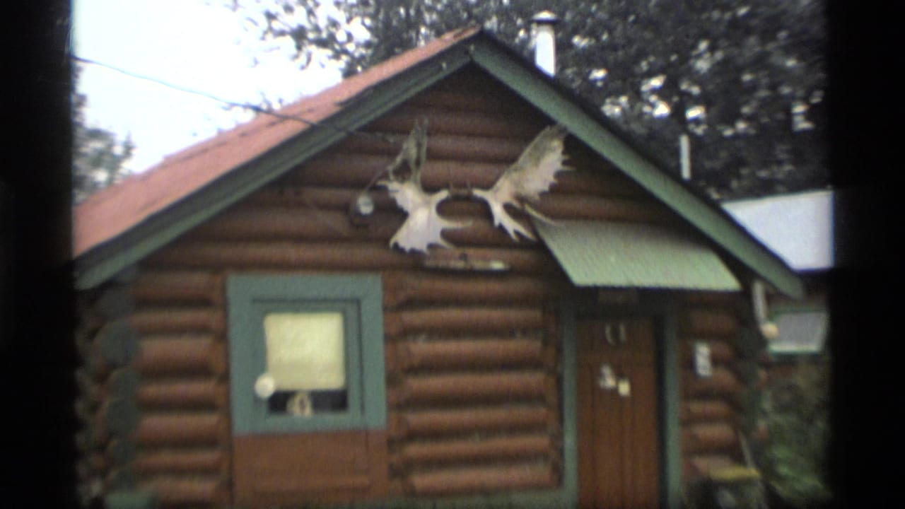 Log cabin exterior with moose antlers mounted near the roof peak.