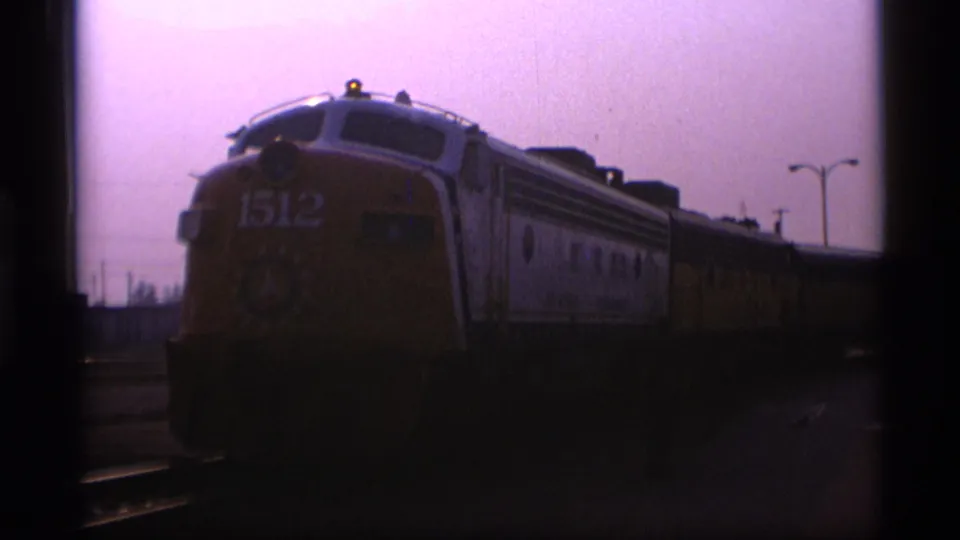 A yellow and white locomotive marked 1512 sits on rail tracks in Alaska, captured in soft 1977 8mm footage.