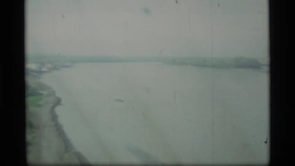 1977 Alaska 8mm frame showing an elevated moving view over a wide river or bay with a curving shoreline below.