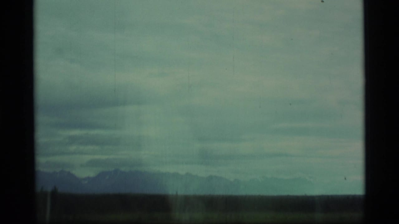 Distant mountains beyond a dark field under a cloudy blue-green sky.