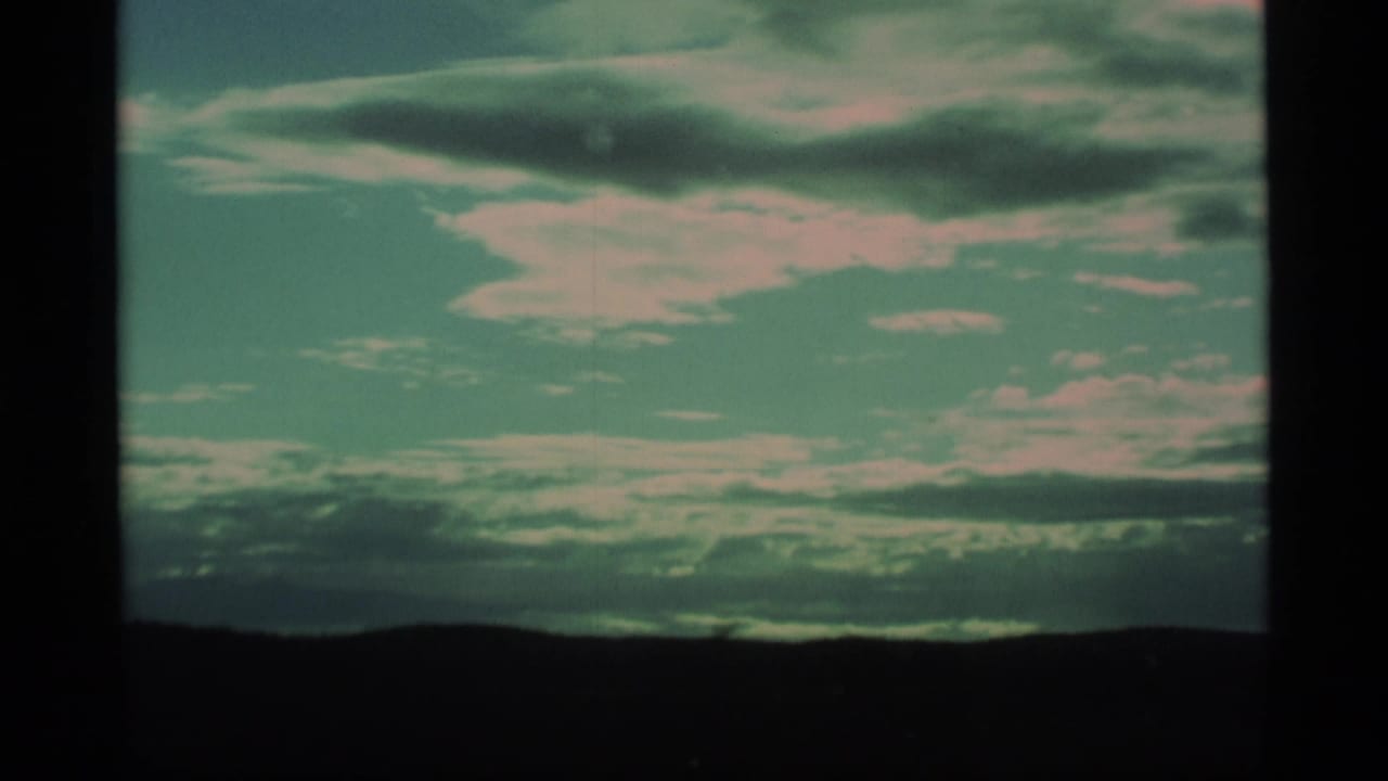 1977 Alaska 8mm frame showing a clouded sky over a dark silhouetted landscape from a moving travel viewpoint.