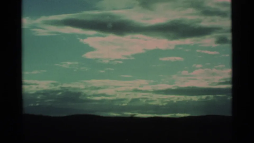 1977 Alaska 8mm frame showing a clouded sky over a dark silhouetted landscape from a moving travel viewpoint.