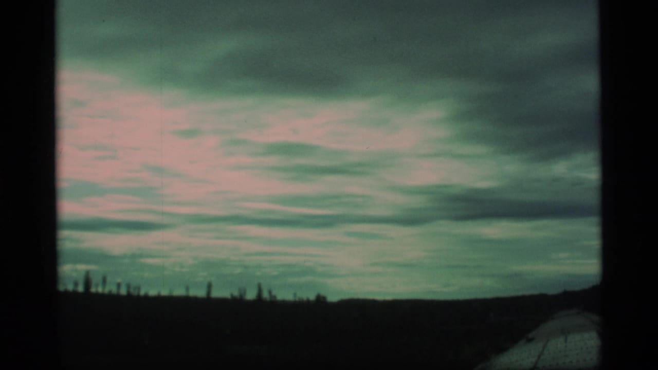 Dramatic clouds above a dark roadside landscape with faint distant tree shapes.