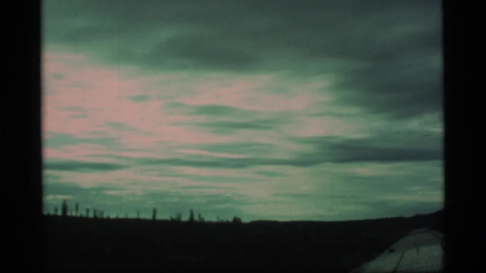 1977 Alaska home-movie frame with heavy clouds, a low dark horizon, and roadside scenery seen in motion.
