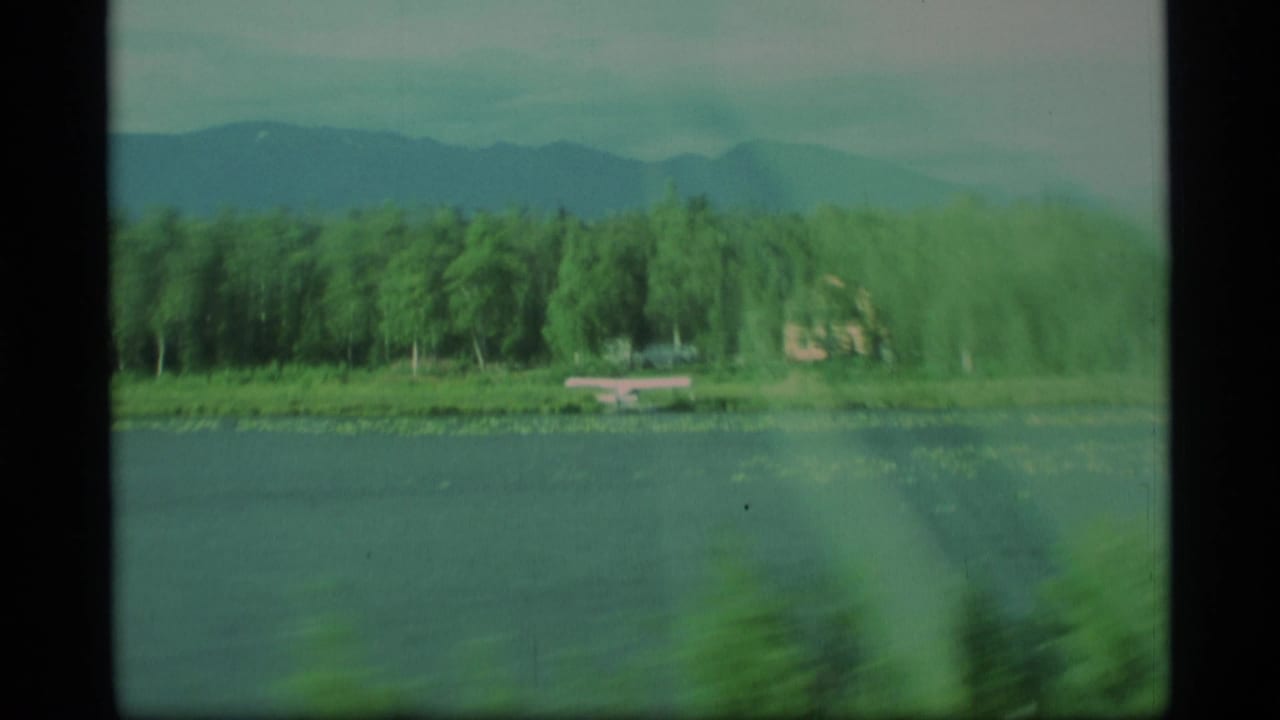 Lake and pine-covered shoreline seen through motion blur with distant mountains beyond.