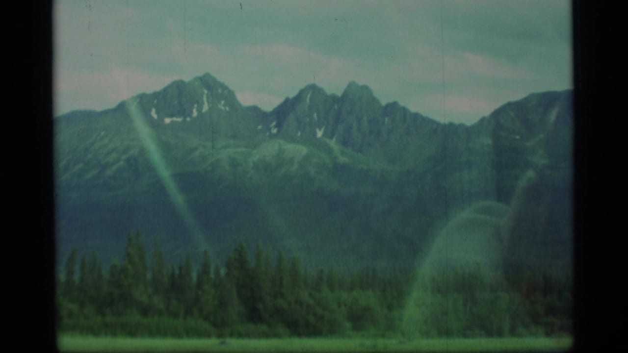 Snow-dusted mountain range above evergreen forest seen through a vehicle window.